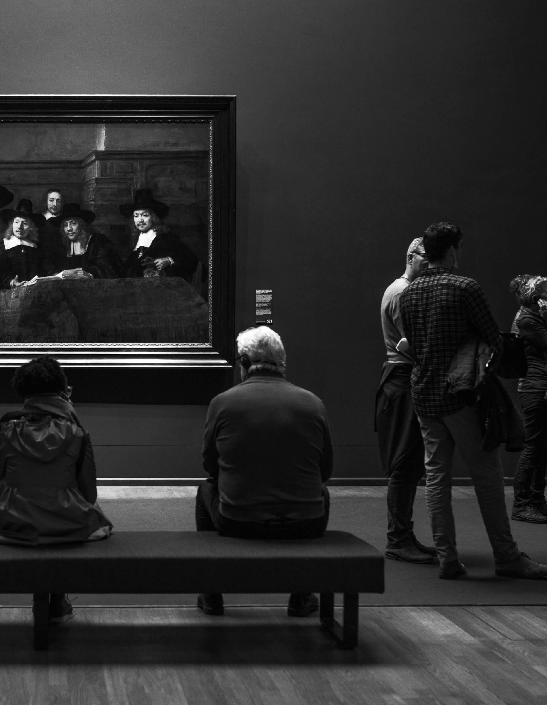 We serve the Art and Culture Community. An older man is looking at a painting inside a museum.